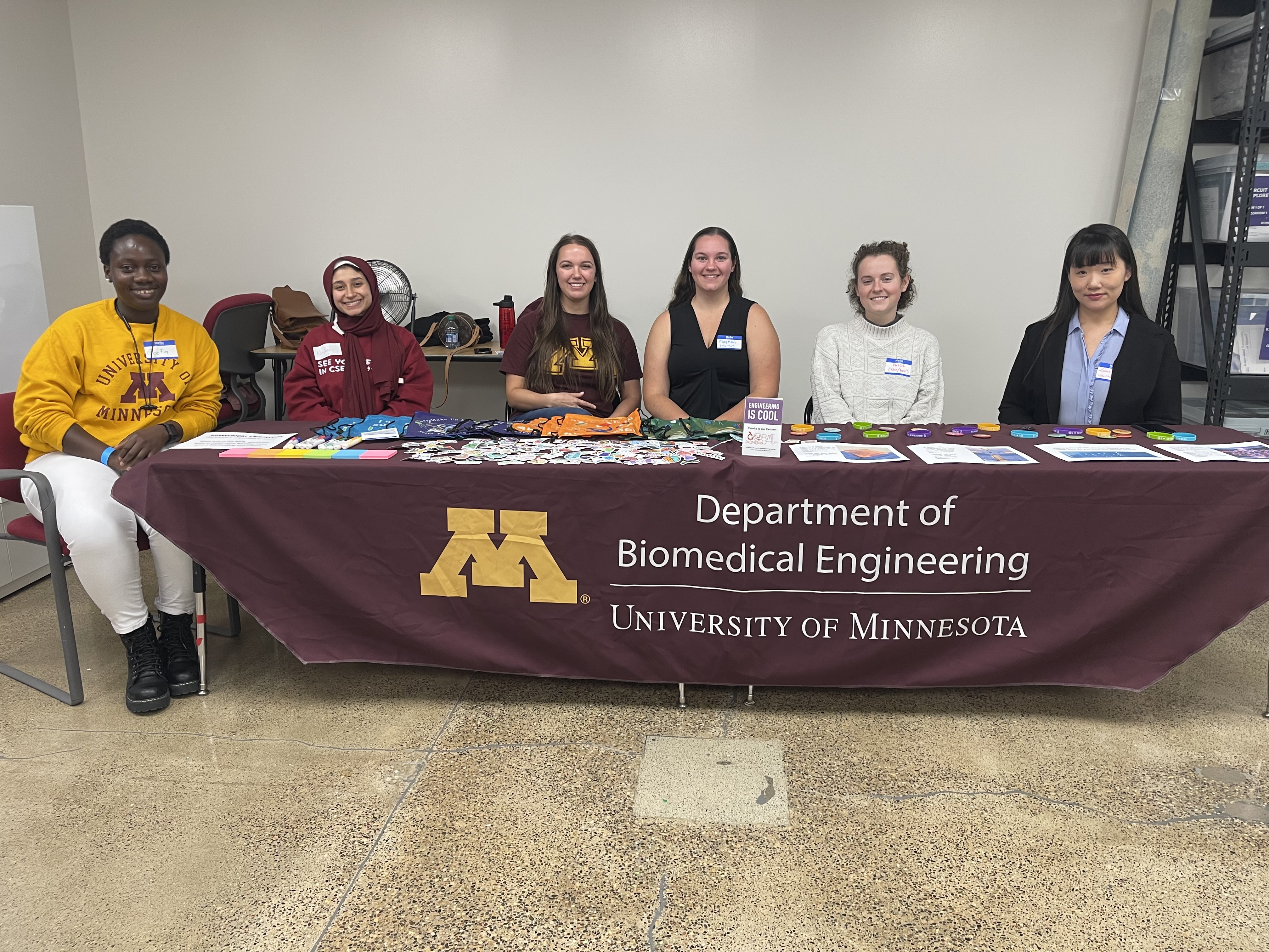 A group of women sit behind a table with a tablecloth that reads "Department of Biomedical Engineering, University of Minnesota"